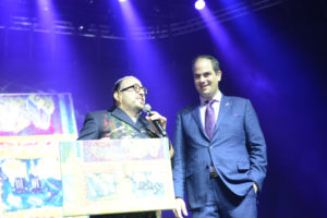 Eli Beer receives the painting from Lipa Schmeltzer on stage at the Annual United Hatzalah United for Life Concert (Credit: Oren Lumenkrantz)